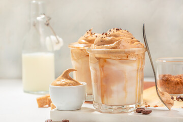 Dalgona cream coffee whipping on cold milk In a transparent glass on light background