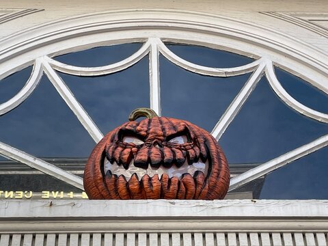 A scary Halloween pumpkin with an evil looking jack o&rsquo;lantern face hangs in front of a window over a door on an autumn day in Salem Massachusetts