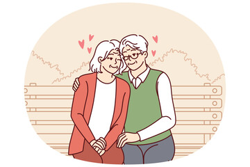 Elderly couple in love sits on park bench hugging and enjoying happy family life. Relationship between elderly man and woman in love sitting hugging and having fun from retirement.