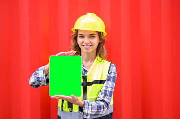 Logistic operators worker shows tablet computer with blank screen, working in cargo container warehouse industry factory site in export, import, and transportation concept. green screen tablet.