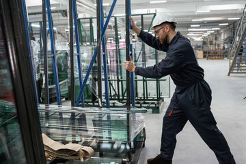 Moving the parts of windows. Factory worker is indoors with hard hat