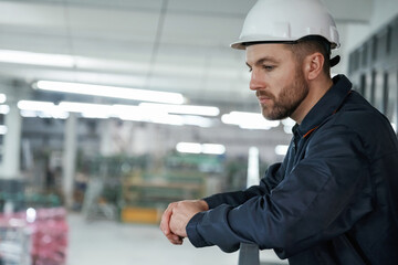 Leaning on the railings. Factory worker is indoors with hard hat