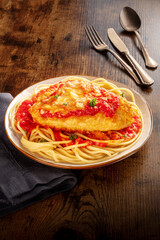 Chicken Parmesan, Italian pasta dish. Breaded chicken breast with cheese and spaghetti with tomato sauce, on a rustic wooden table with cutlery