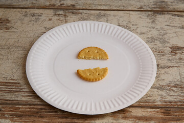One broken cookie on a disposable plate on a wooden background, close-up, rising food prices,...