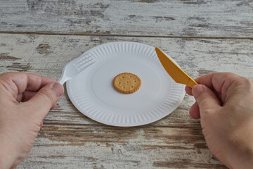 A hand holding a fork and knife over a plate of one cookie close-up, rising food prices,...