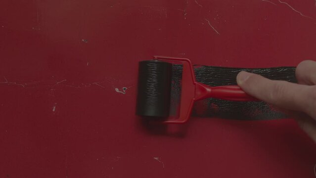 hand holding a red paint roller, black lino ink remain, linocutting paint roller texture on red photo paper background, 4k and 50p.