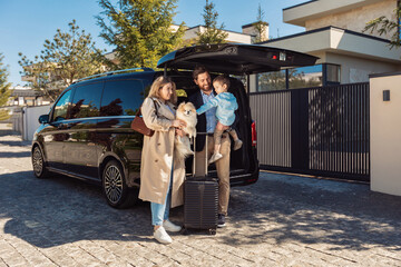 A young stylish family with their son and dog, stands near taxi trunk with luggage