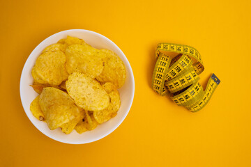 Potato chips and tape measure on a colored background. Diet and proper nutrition concept. Salty...