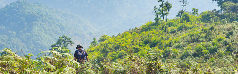Traveler men with backpack walking on path in the tropical forest. Web banner size.