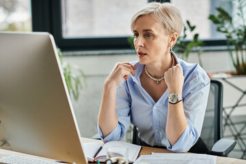 Middle-aged businesswoman with short hair diligently works on her laptop during menopause symptoms in the office.