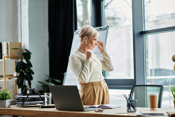 Middle-aged businesswoman with short hair stands confidently in front of a laptop computer in a...