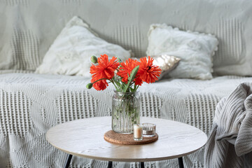 A minimalistic composition with red poppy flowers in a vase and candles at home.