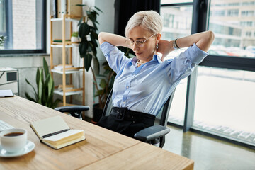 Middle-aged businesswoman with short hair sitting at desk, hands behind head, deep in thought and...