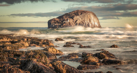 Horizontal image of Bass Rock, Scotland's east coast, from a rocky shore with sun shining on...