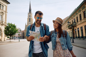 Happy couple of tourists reading map while walking through  city.