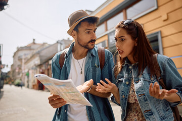 Confused couple of tourists examining map while exploring  town.