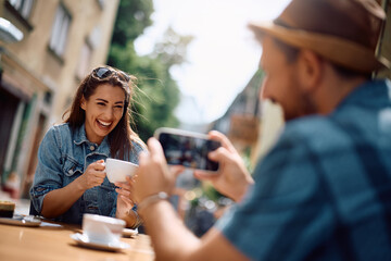 Young woman having fun while her boyfriend is photographing her in  café.