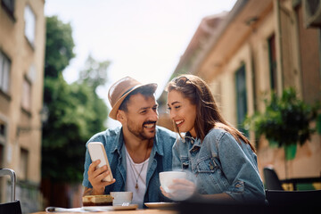 Happy couple using cell phone while drinking coffee in city.