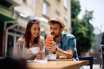 Young couple text messaging on mobile phone at sidewalk café.