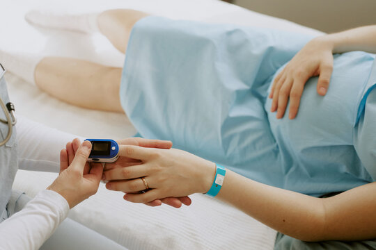 Nurse holding pregnant patients hand and examining her saturation with help of pulse oximeter