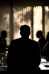 A group of silhouetted people in a business meeting with light streaming through a window in the background