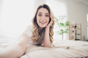 Photo of positive cheerful girl lying bed make selfie in room interior