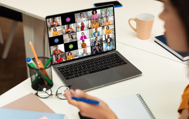 A laptop screen displays a video conference call with multiple participants of various backgrounds and ethnicities, all appearing in separate video squares.