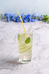 Cucumber drink with basil leaves, ice cubes and a cocktail straw.