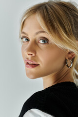 A stylish young woman with blonde hair donning a black and white shirt against a grey backdrop.