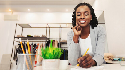 African American woman is seated at a desk, engaged in writing on a piece of paper. She appears focused and intent on the task at hand, concentrating on the text, copy space