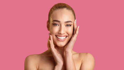 A young woman with blonde hair smiles brightly at the camera. Her hands are gently touching her...