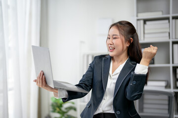 Businesswoman celebrating success in office while looking at laptop screen. Professional achievement, excitement, motivation concept.