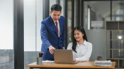 Businessman and businesswoman working together in modern office, discussing project on laptop.