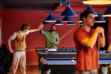 Friends enjoy a game of pool in a brightly lit pool hall.