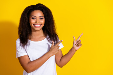 Portrait of nice young woman indicate fingers empty space wear t-shirt isolated on yellow color background