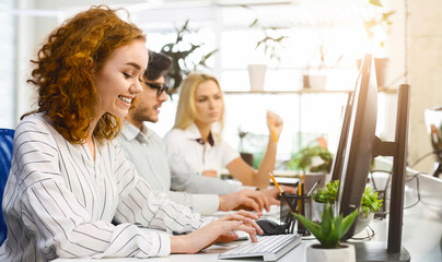 Several coworkers are seated at a desk, each engrossed in their computer screens, actively typing...
