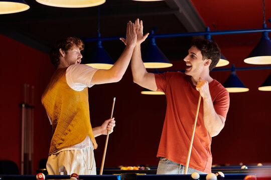 Friends give each other a high five after a game of billiards. - Powered by Adobe