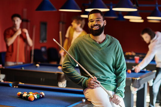 A man smiles while holding his pool cue, enjoying a casual game of billiards with his friends.