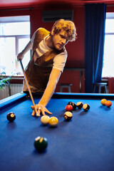 Fototapeta premium A man takes aim at the billiard balls on the green felt table.