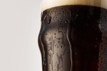 Pint glass filled with dark, cold, foamy craft beer with droplets on condensation on glass against...