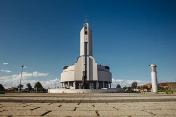 A modern white church with a tall steeple and a clock, photographed from a low angle under a clear blue sky, capturing its architectural beauty and serene surroundings.