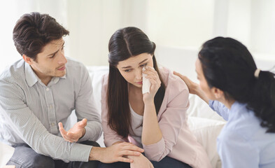 Fototapeta premium A distressed woman with a tissue is being comforted by husband and therapist in a bright, modern living room during the day, offering support and understanding in her time of need.