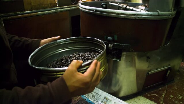 Coffee shop owner using sift to clean roasted coffee beans to sell them.
