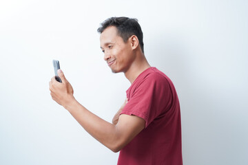 a young man wearing a red t-shirt holding a cellphone is calling happy expression on an isolated white background