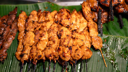 Group of grilled BBQ chicken meat in wooden skewers, placed on banana leaf at local market. Street food object photo, close-up.