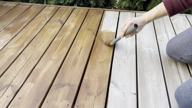 A man is painting wooden deck