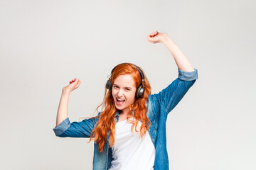 A woman wearing headphones stands with her arms lifted in the air, seemingly enjoying the music she...