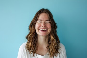 Fototapeta premium Portrait of a joyful caucasian woman in her 20s smiling at the camera while standing against pastel blue background