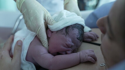 Close-up of Newborn baby after birth, first seconds of life, nurse's hand putting warm clothes,...