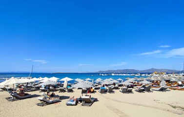 Photo of people lounging under the straw umbrellas, at the idyllic Skala beach on Agistri island,...